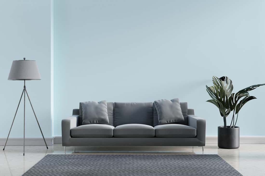 Luxury modern interior of blue pastel and gray tone living room home decor concept background. Three legs electric lamp and monstera pot on marble floor and mat.