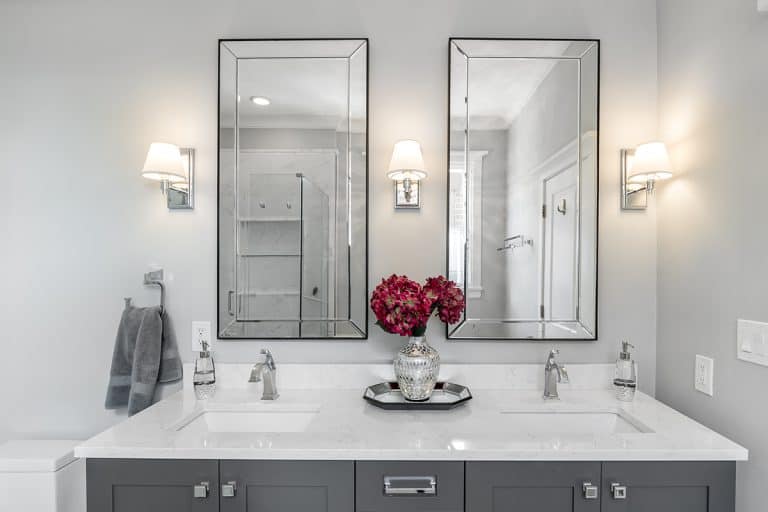 A luxurious bathroom with a grey double vanity with flowers sitting on the white quartz counter top, How To Vent A Double Vanity [Step By Step Guide]