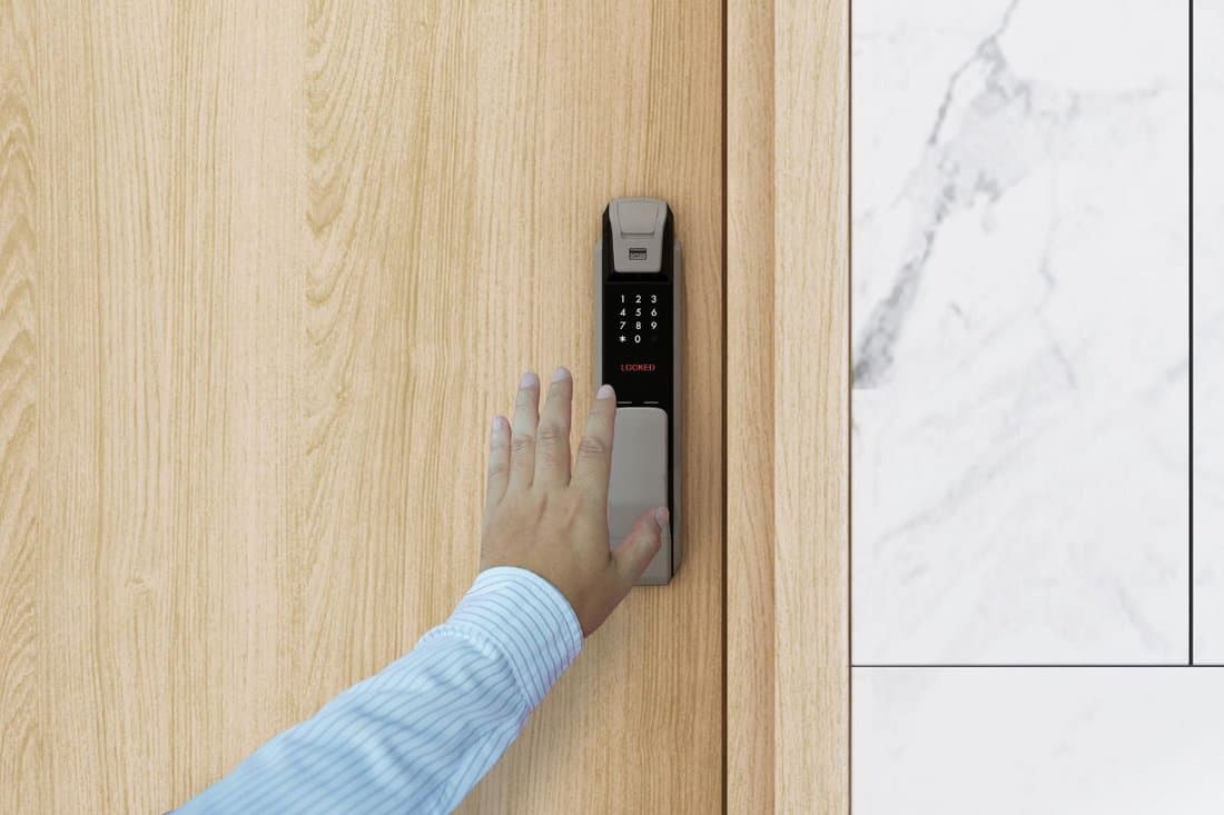Man or woman's finger entering password code on digital door lock touch screen keypad entry in front of the room.