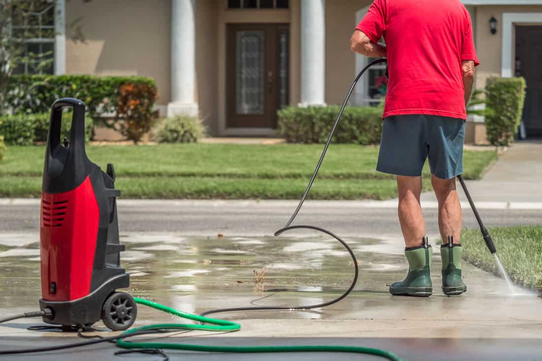 Man using electric powered pressure washer to power wash residential concrete driveway