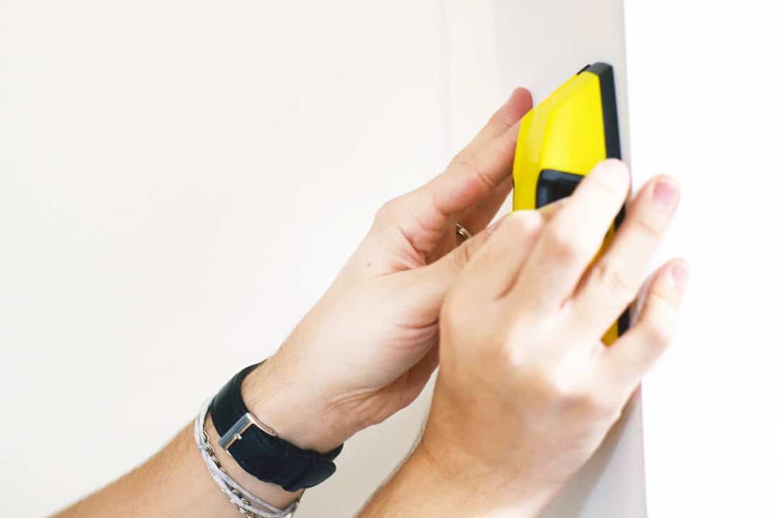 Man using stud finder to search apartment wall for studs and live wires