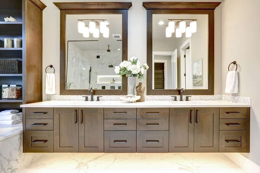 Master bathroom interior in luxury modern home with dark hardwood cabinets, white tub and glass door