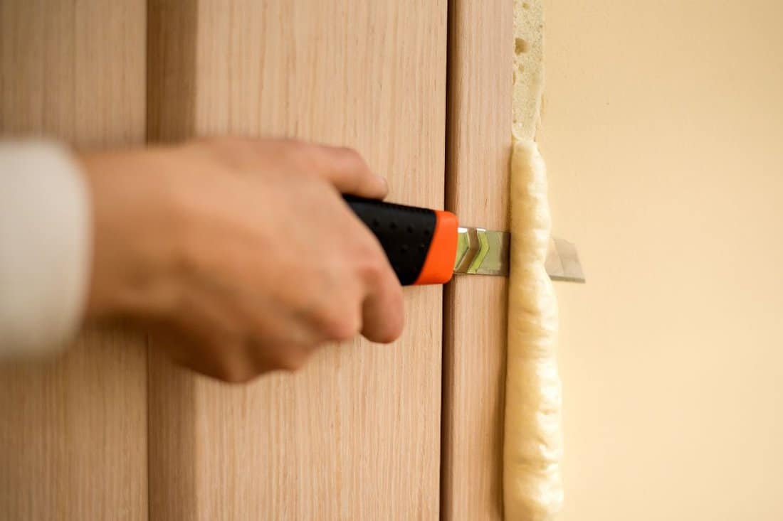 Master knife cuts off excess foam. Installation of doors using polyurethane foam mounting. Cylinder Foam. insulation, Foam construction