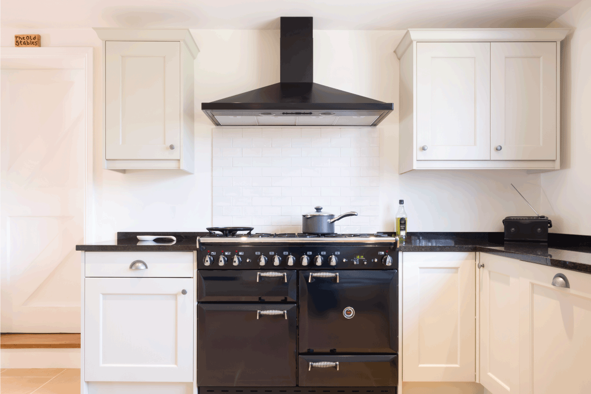 Modern modular kitchen interior in black and off white, with range cooker and chimney extractor hood. How High Should Vent Hood Be Above Stove