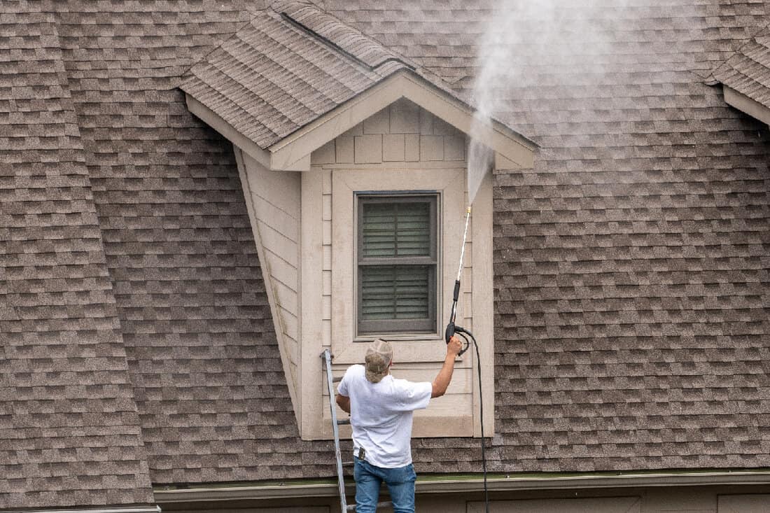 Painter pressure wash spray to clean roof shingles