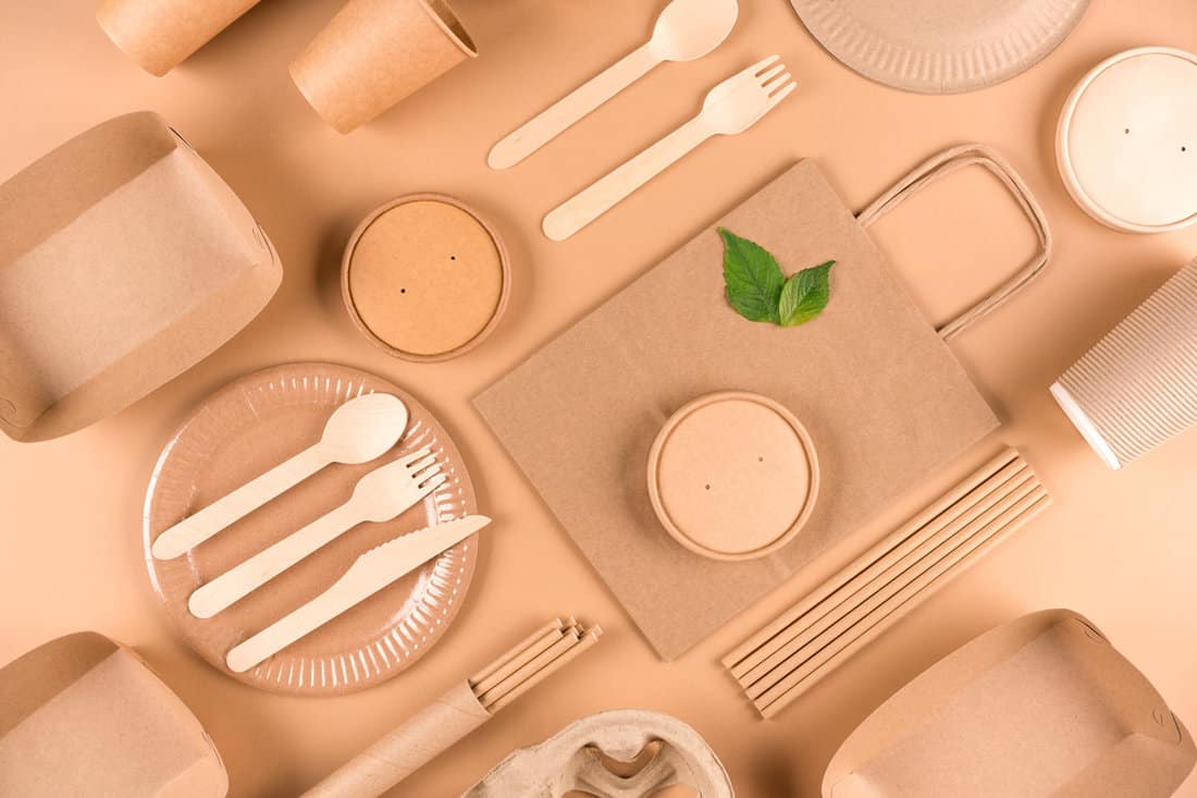Paper utensils and wooden cutlery set over light brown background. Street food sustainable paper packaging, zero waste packaging concept