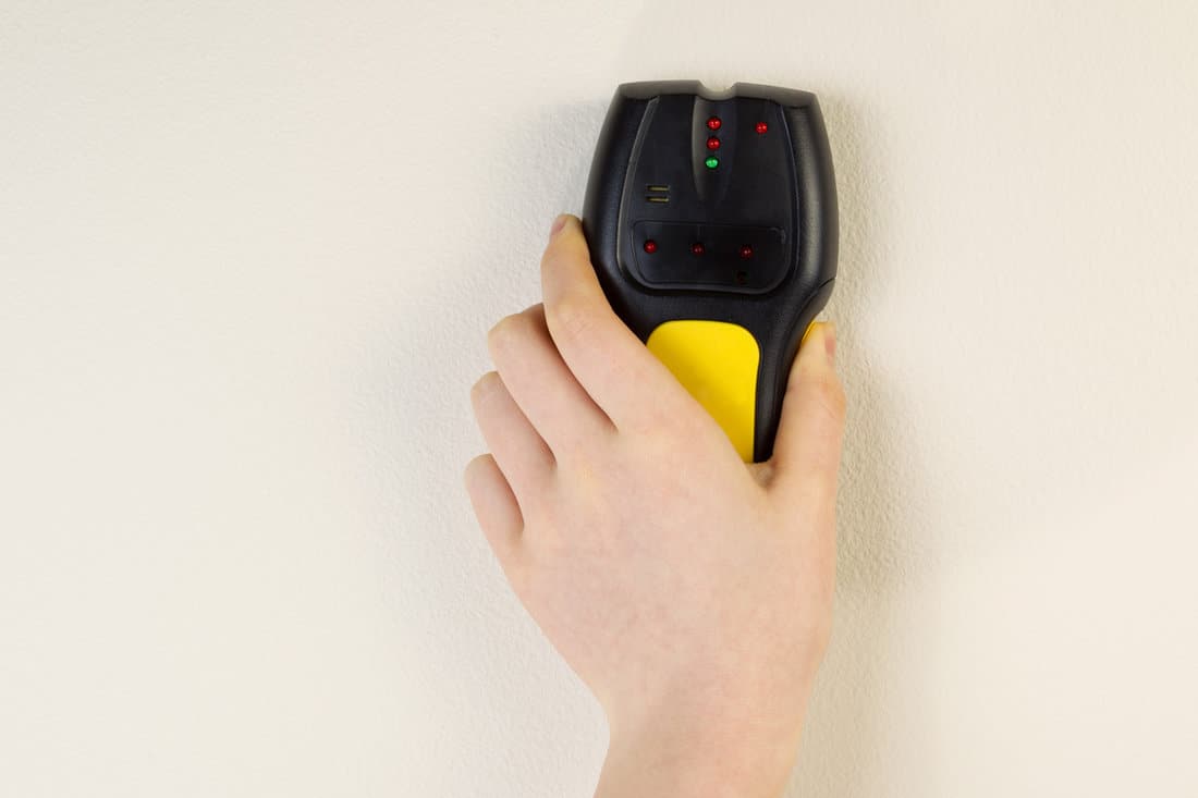Photo of female hand holding stud finder against interior home white wall