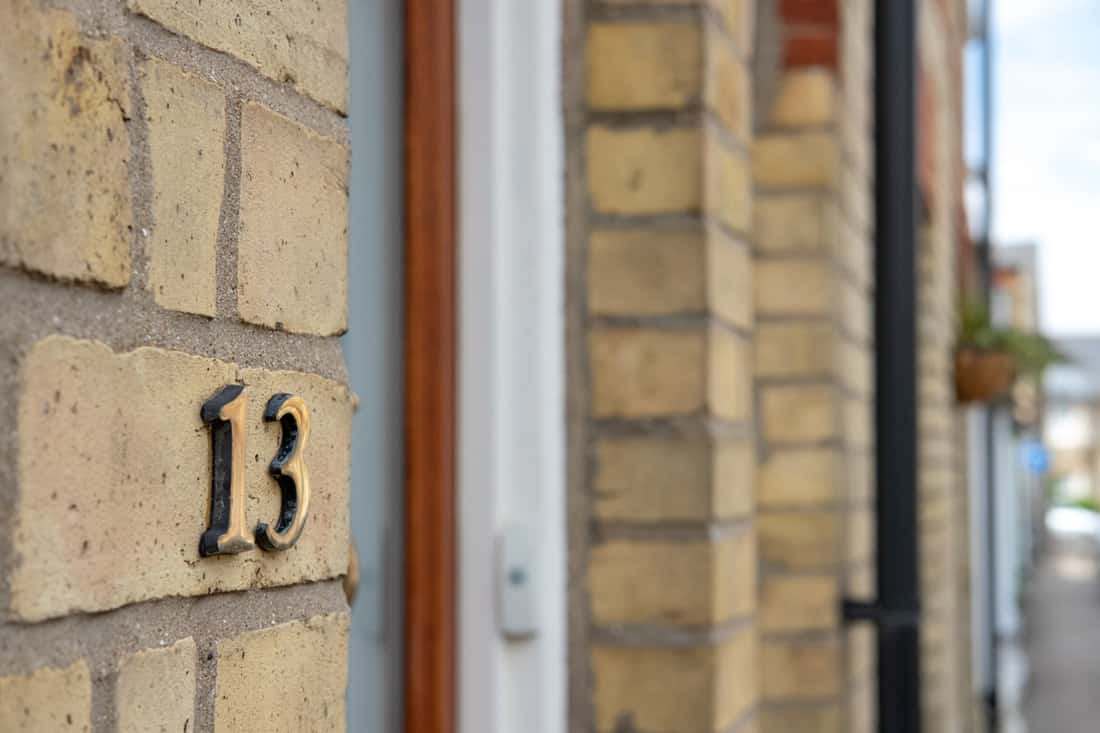 Shallow focus view of a brass number 13 number seen attached to the entrance of a brick-built terraced house in this english market town.
