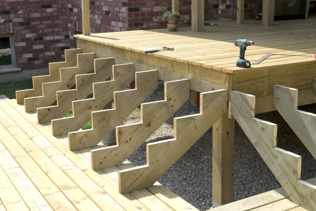 Stair stringers made from pressure treated wood being temporarily positioned during backyard deck construction.