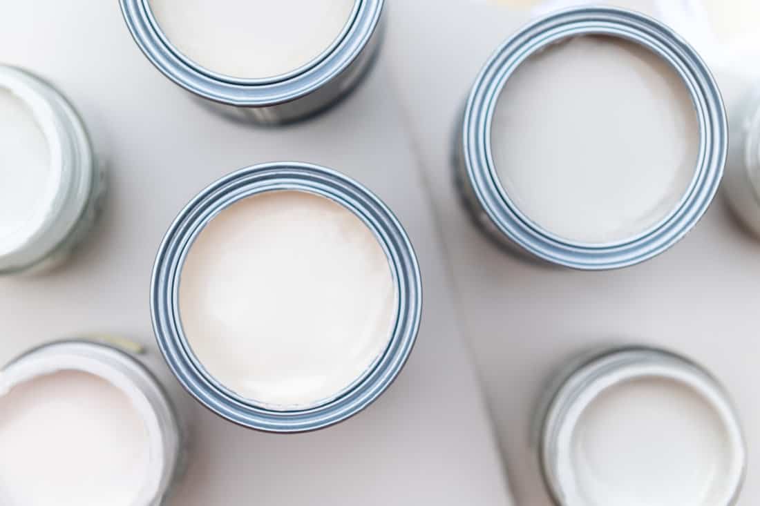 Tiny sample paint cans during house renovation, process of choosing paint for the walls, light grey and pastel colors, color charts and unit samples on background