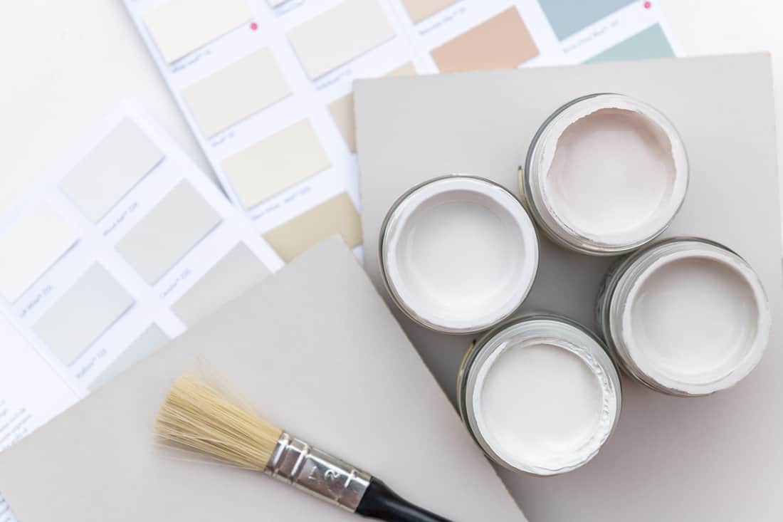 Tiny sample paint pots during house renovation, process of choosing paint for the walls, light grey and pastel colors, color charts and unit samples on background