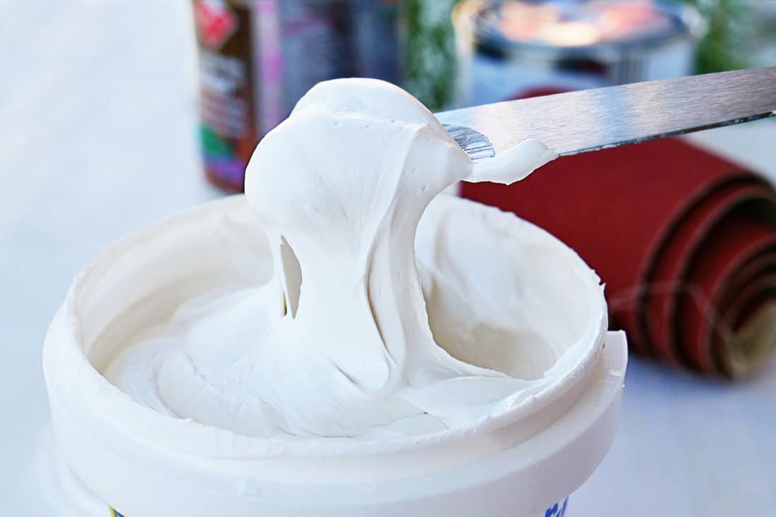 White acrylic glazing putty for wood and metal, interior and exterior use on a putty knife showing the paste consistency. 