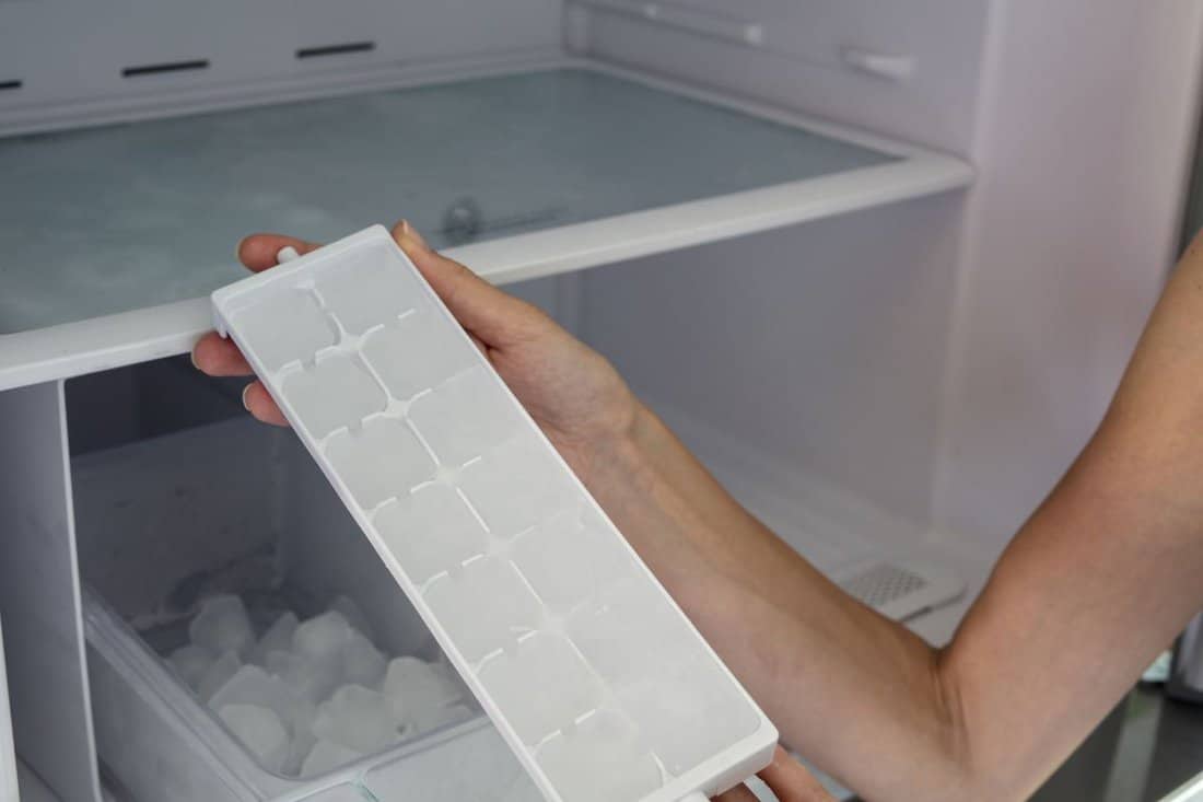 Woman hands taking ice cubes from fridge close up