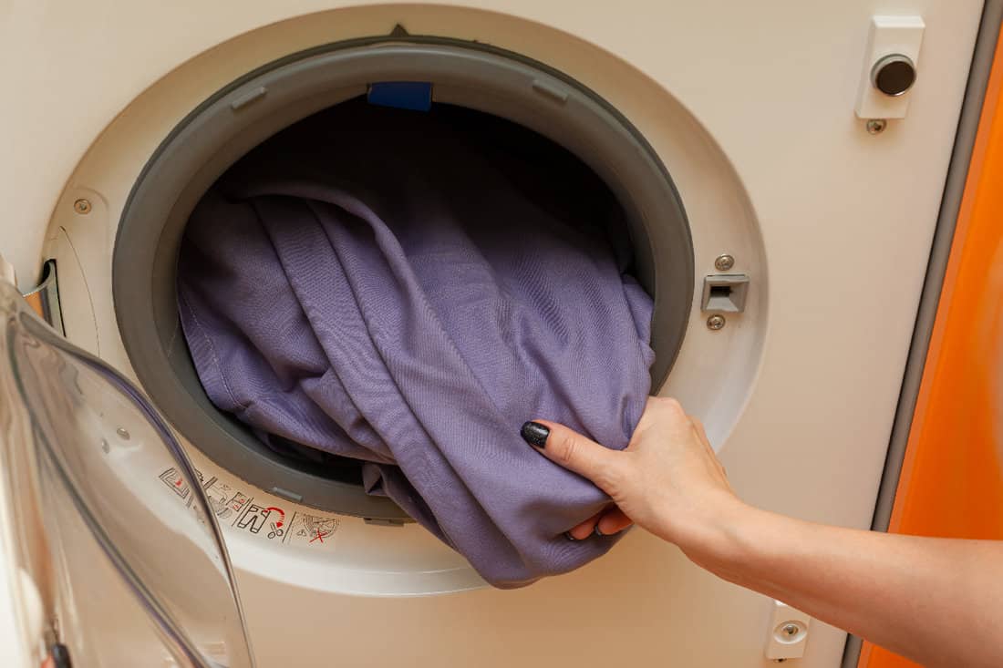 Woman's hand pulls out laundry from the washing machine
