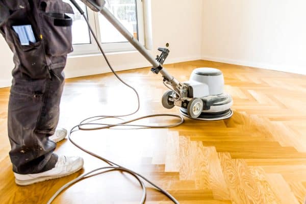 Worker polishing the parquet flooring, Does Sandless Floor Refinishing Work [& How To]?