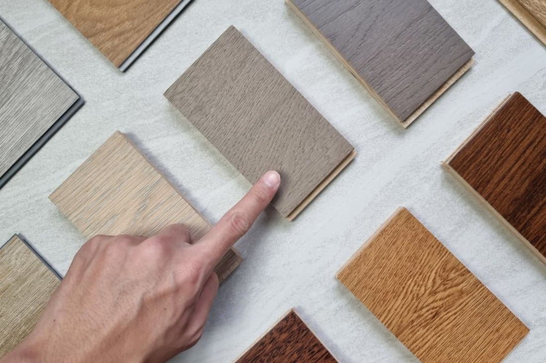 designer's hand choosing samples of interior wooden flooring material consists oak, walnut, ash, douglasfir engineering (or laminate) flooring, ash and oak vinyl tile. top view of selected material