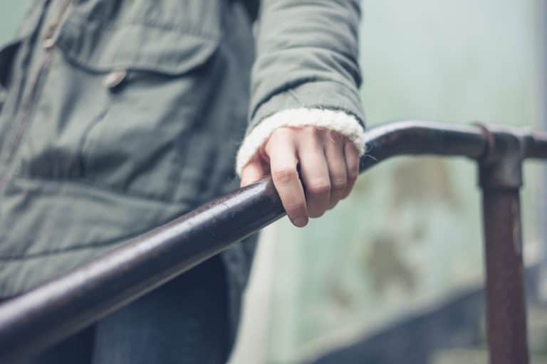 hand-woman-holding-on-metal-banister, What Kind Of Paint & Finish To Use On Handrails? [Inc. Tips & Tricks]