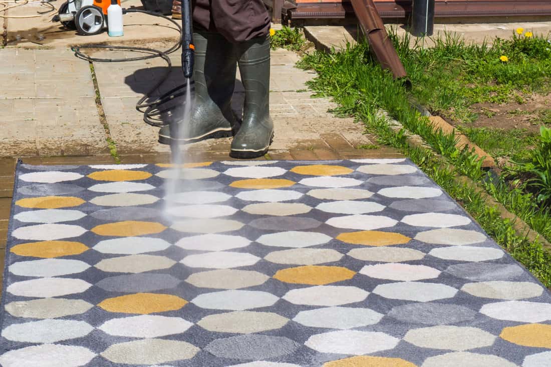 man washing carpet with pressure washer outdoors