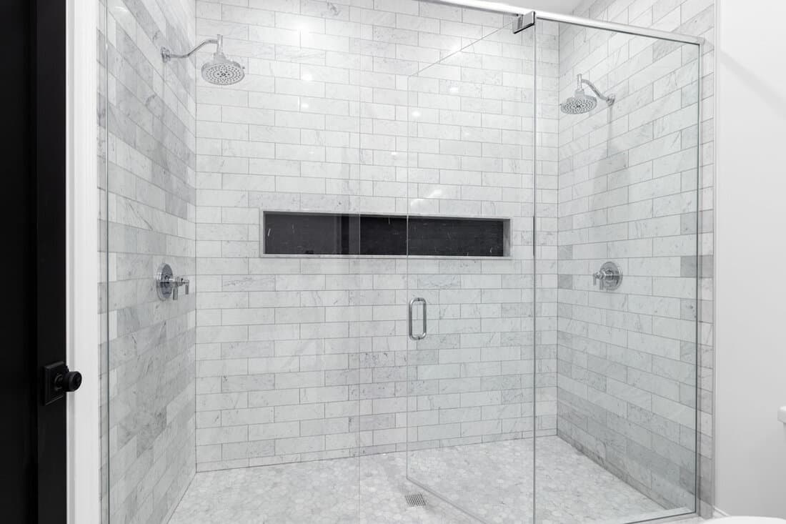 A large, luxury double shower with marble subway tile walls, marble hexagon floor, and black hexagon tile