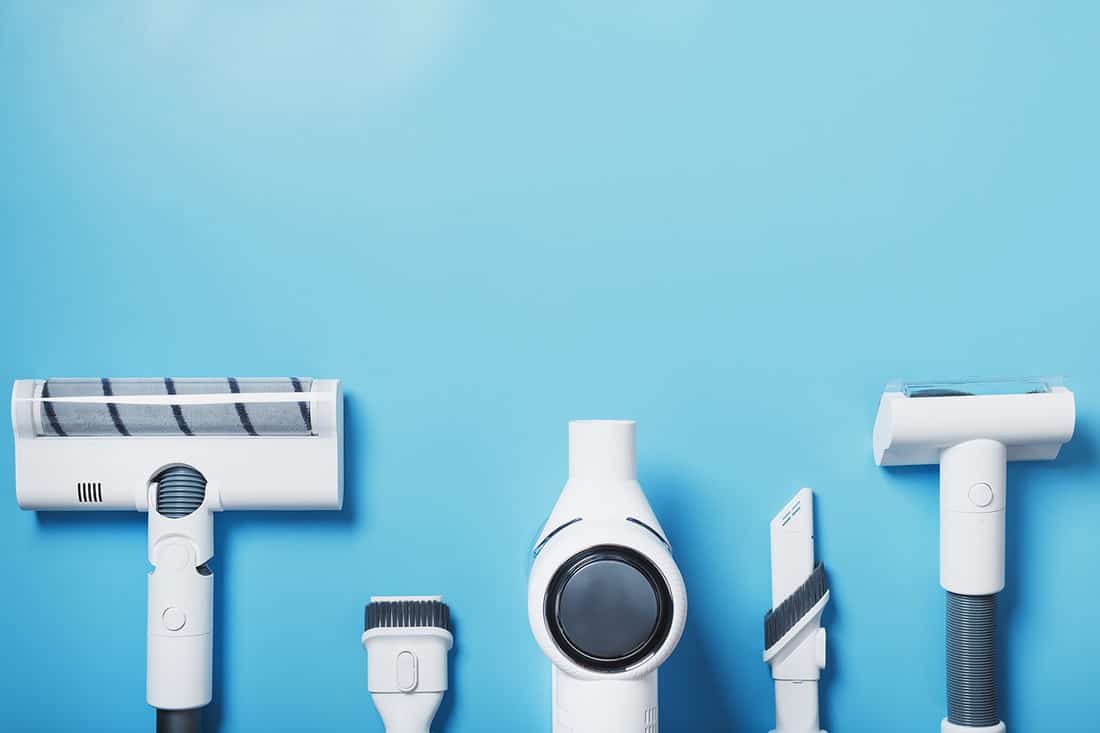 A set of nozzles and a white cordless vacuum cleaner in a row on a blue background