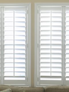 A set of open white plantation shutters in a light butter yelllow room - Should You Put Shutters On A Picture Window