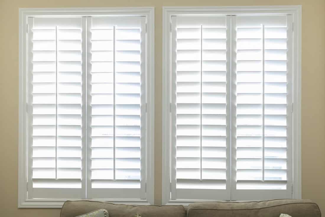 A set of open white plantation shutters in a light butter yellow room