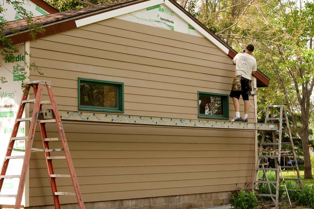 A worker installs Hardie Board siding and flashing to an existing structure.