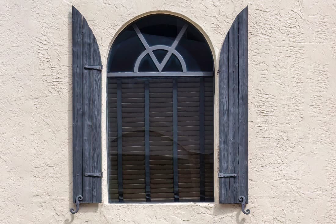Arched window with vintage wooden storm shutters on bright exterior stucco wall of a building
