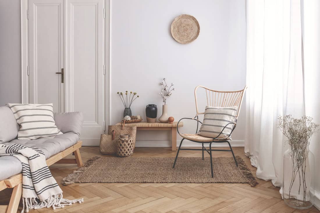 Armchair on rug next to bench with plants in white loft interior with wooden sofa