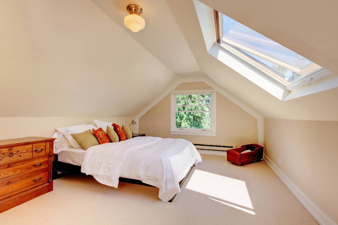 Attic modern bedroom with white bed and skylight and beige walls and carpet