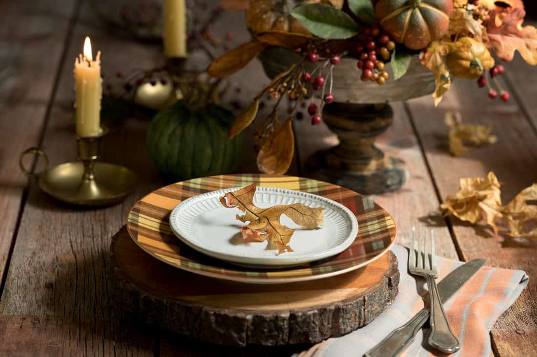 Autumn dining table place setting with pumpkins, gourds and holiday decor arranged on an old wood table 