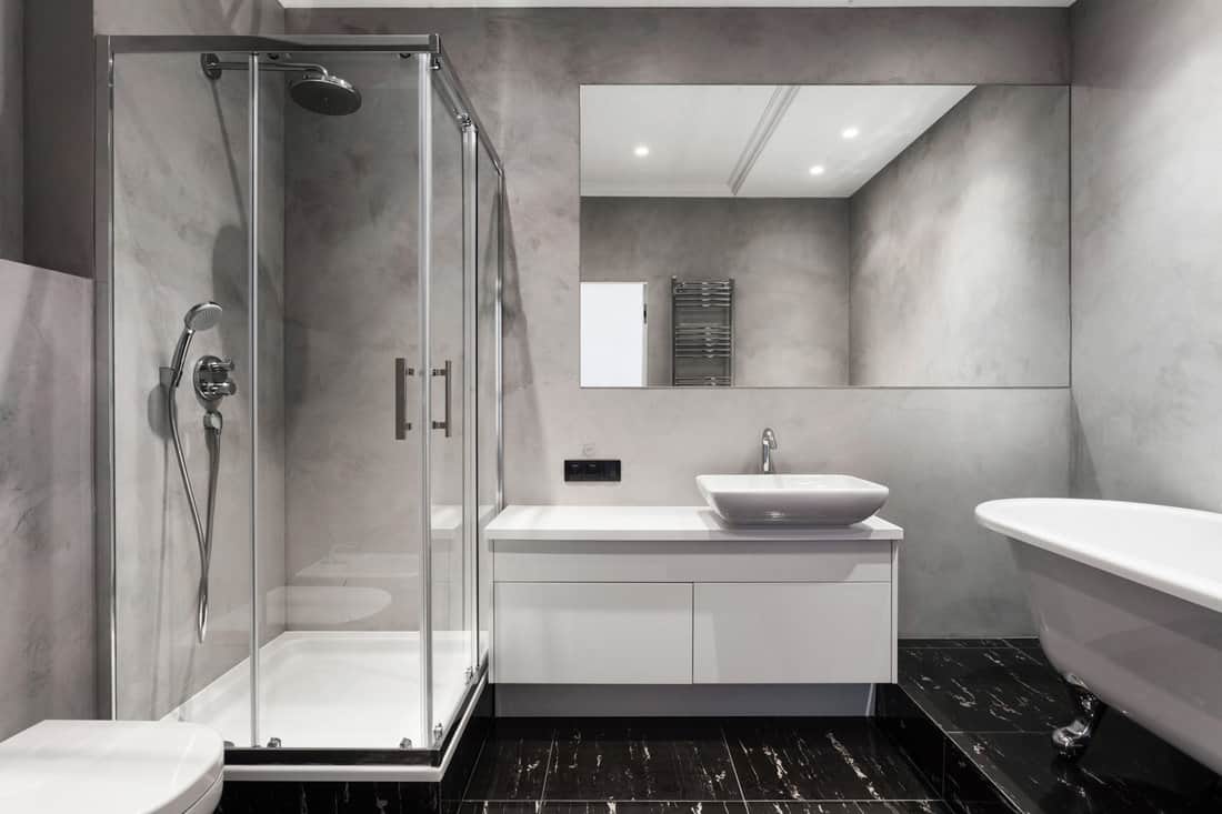 Bathroom with basin, shower cabin, large mirror and chrome silver heater or towel radiator at grey wall. Loft style in new apartment. Modern house with contemporary interior 