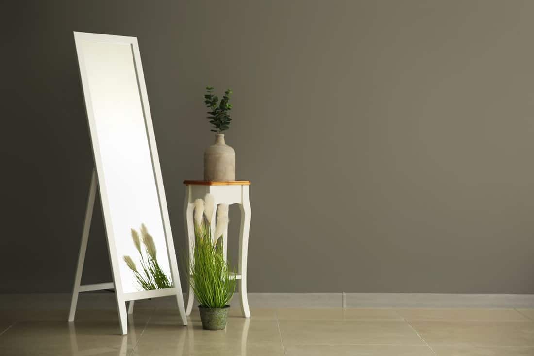 Big mirror and stand with vase near color wall