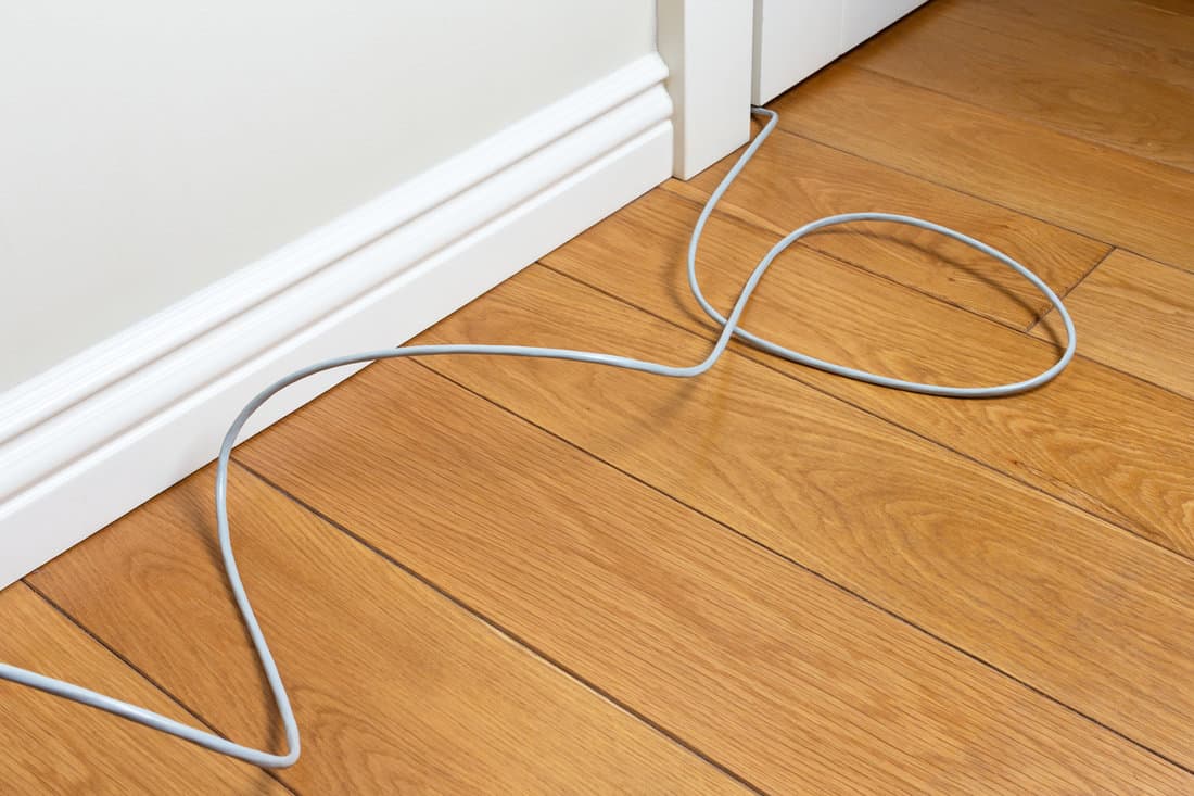 connecting patch cord on the parquet floor of the room along the wall. uncomfortable wiring internet in the apartment. Benefits and usability of Wi-Fi wireless technology 