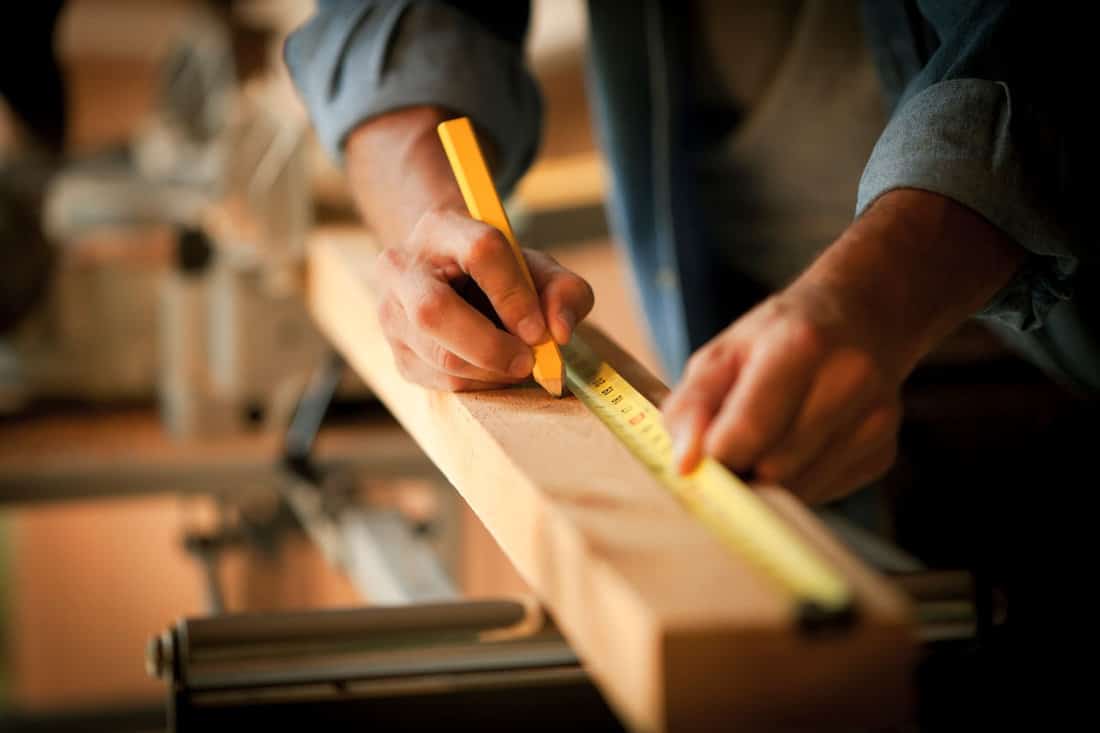 Carpenter Measuring a Wooden Plank using a tape measure