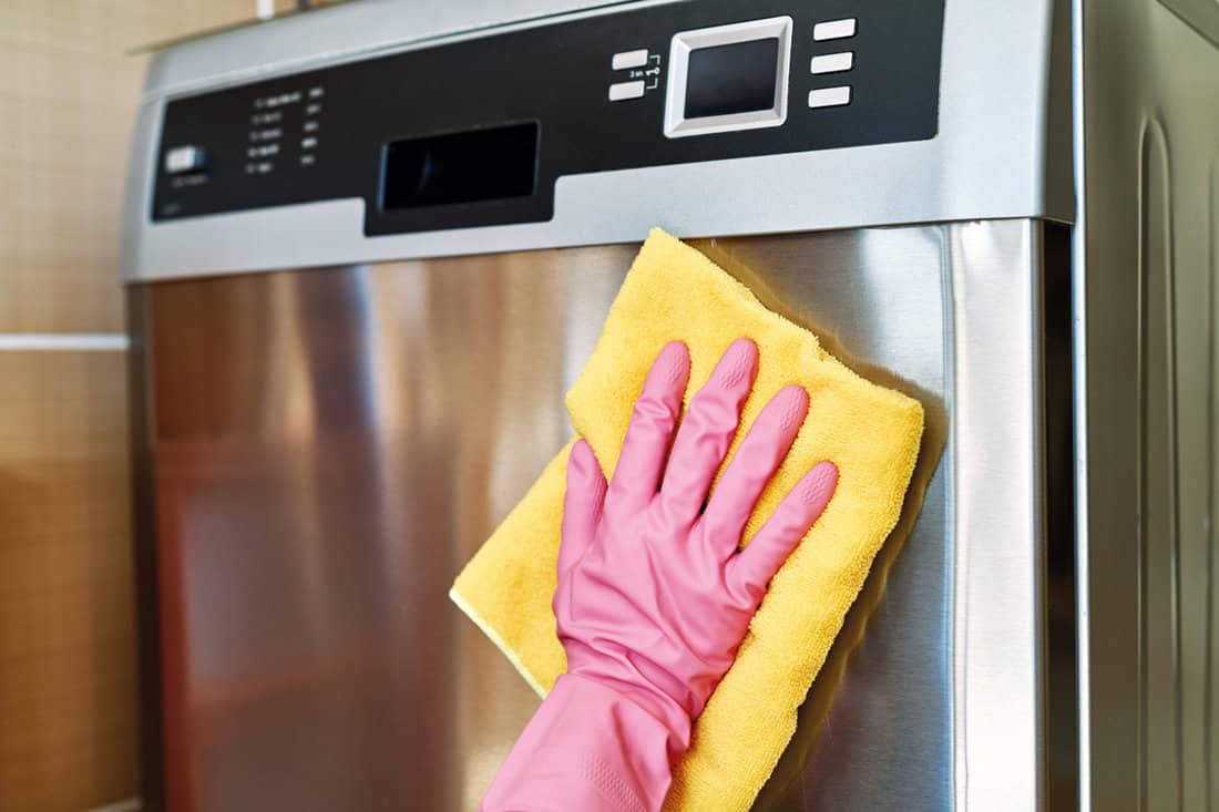Cleaner wearing pink gloves and wiping a yellow cloth to clean the dishwasher