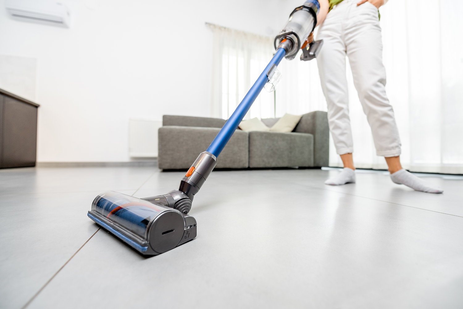 Cleaning floor with cordless vacuum cleaner in the modern white living room