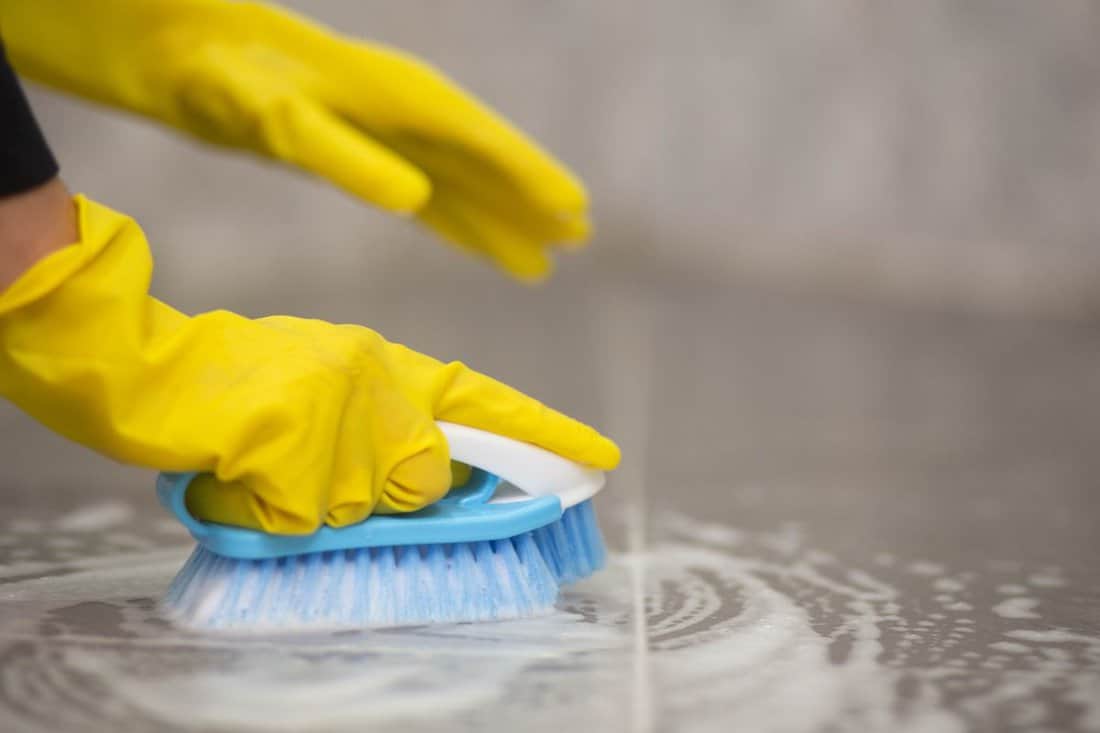 Close-up of a woman's hand using a brush to scrub the tile floor