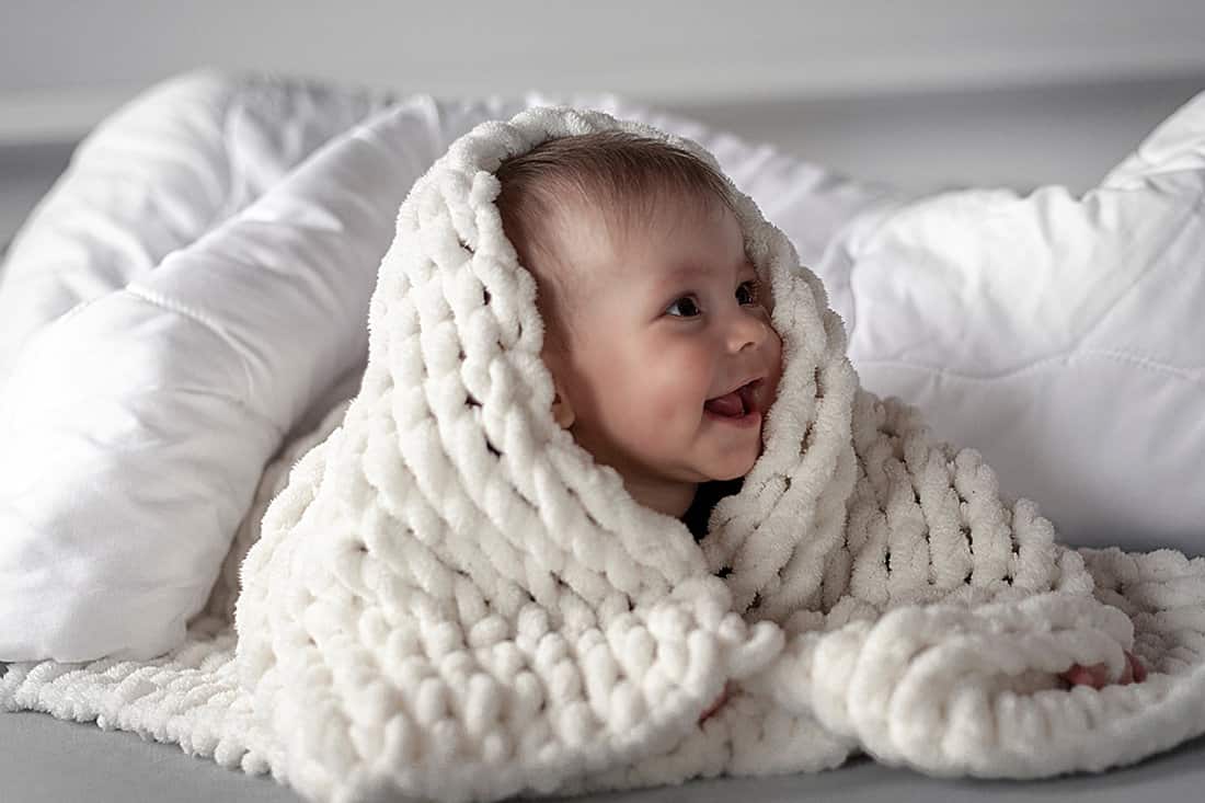 Cute baby girl in bed under a soft merino wool blanket