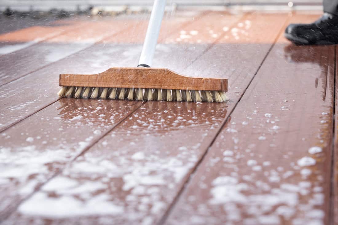 Detail of a scrubbing brush during spring cleaning on a wooden terrace with soap and splashes of water 