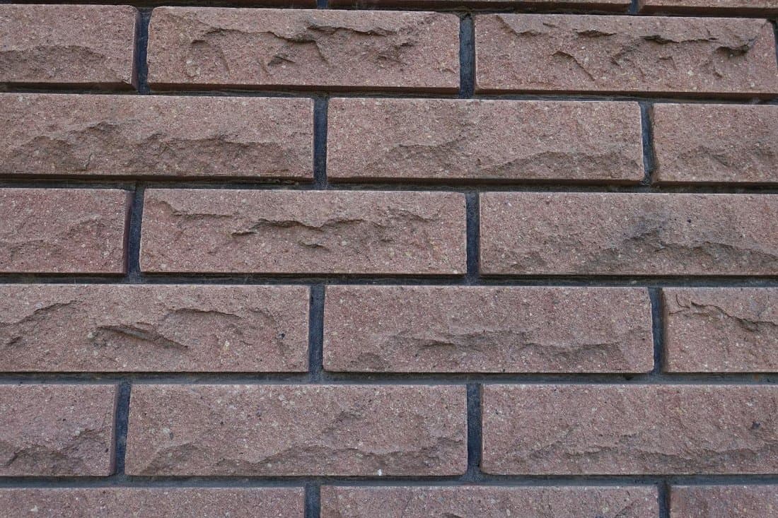 Front view of brown brick veneer wall with black mortar joints 