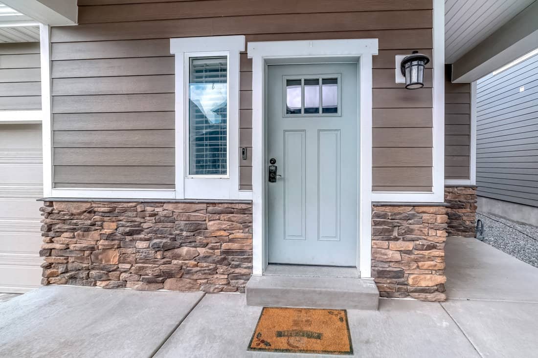 Glass paned front door and sidelight against brick wall and wood siding of home 