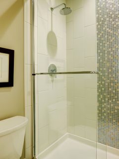 Glass walk-in shower with white subway tiled surround accented with vertical mosaic tile strip in brand-new home bathroom.
