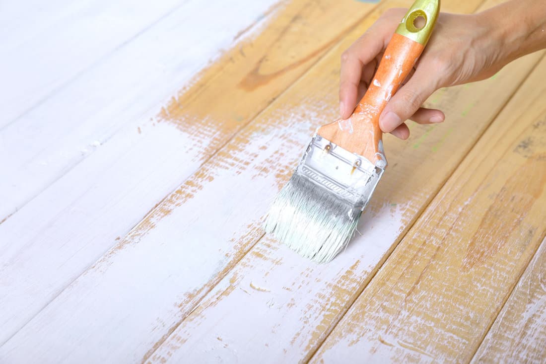 Hand holding paint brush and painting on wood wall with white color.