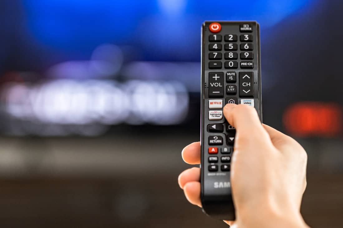 Hand holding remote control showing Netflix and selection of streaming channels with blurred display background