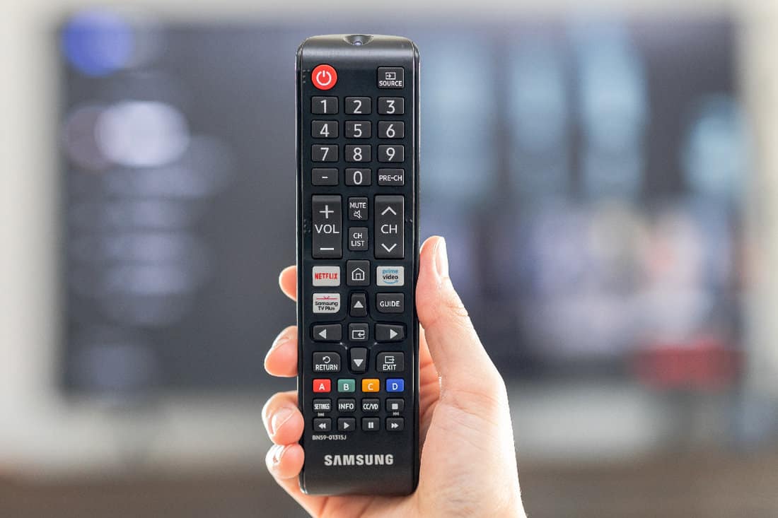 Hand holding remote control showing streaming channel selection for movies and entertainment programs at home