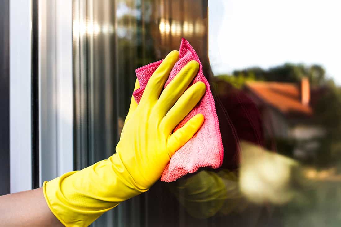 Hand with protective glove cleaning the glass window pane