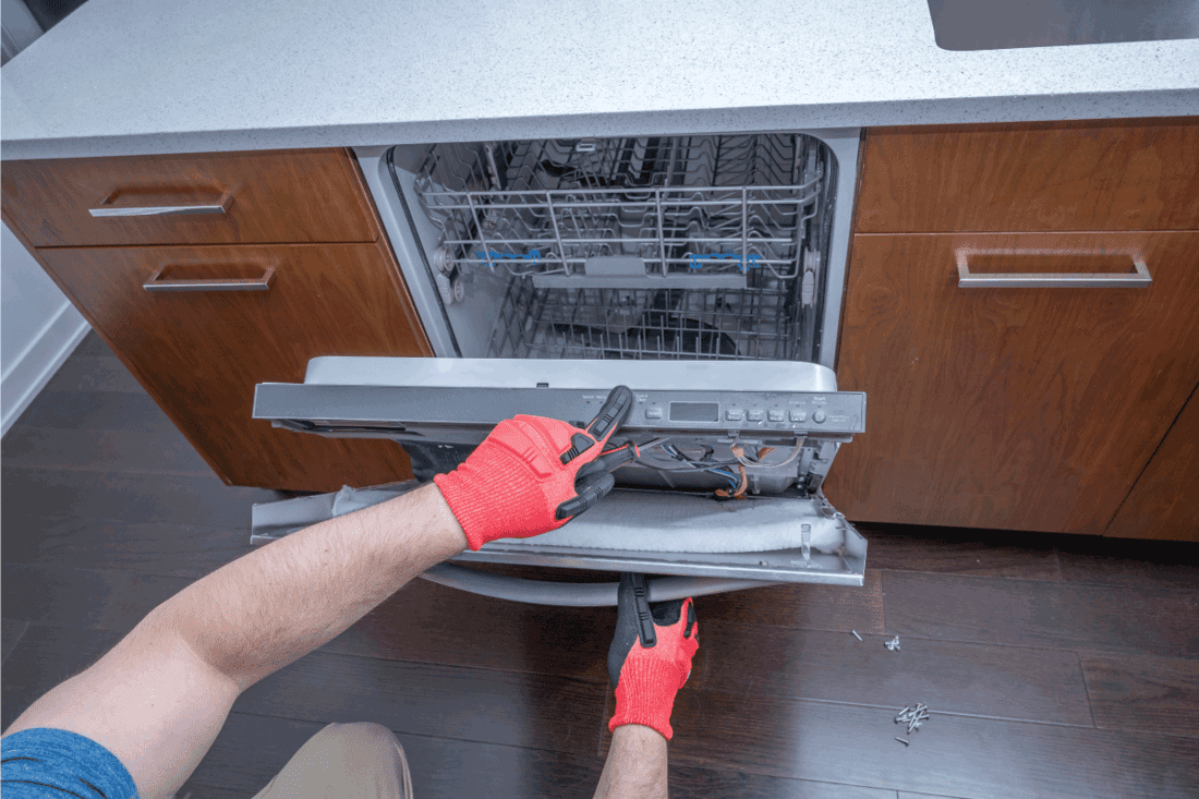 Hands taking apart and repairing a dishwasher inside of a home