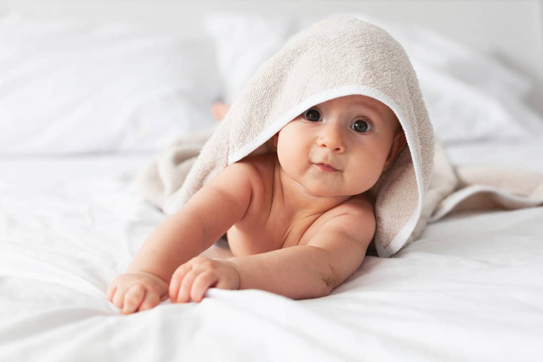 Happy laughing baby wearing biege towel on parents bed after bath or shower.