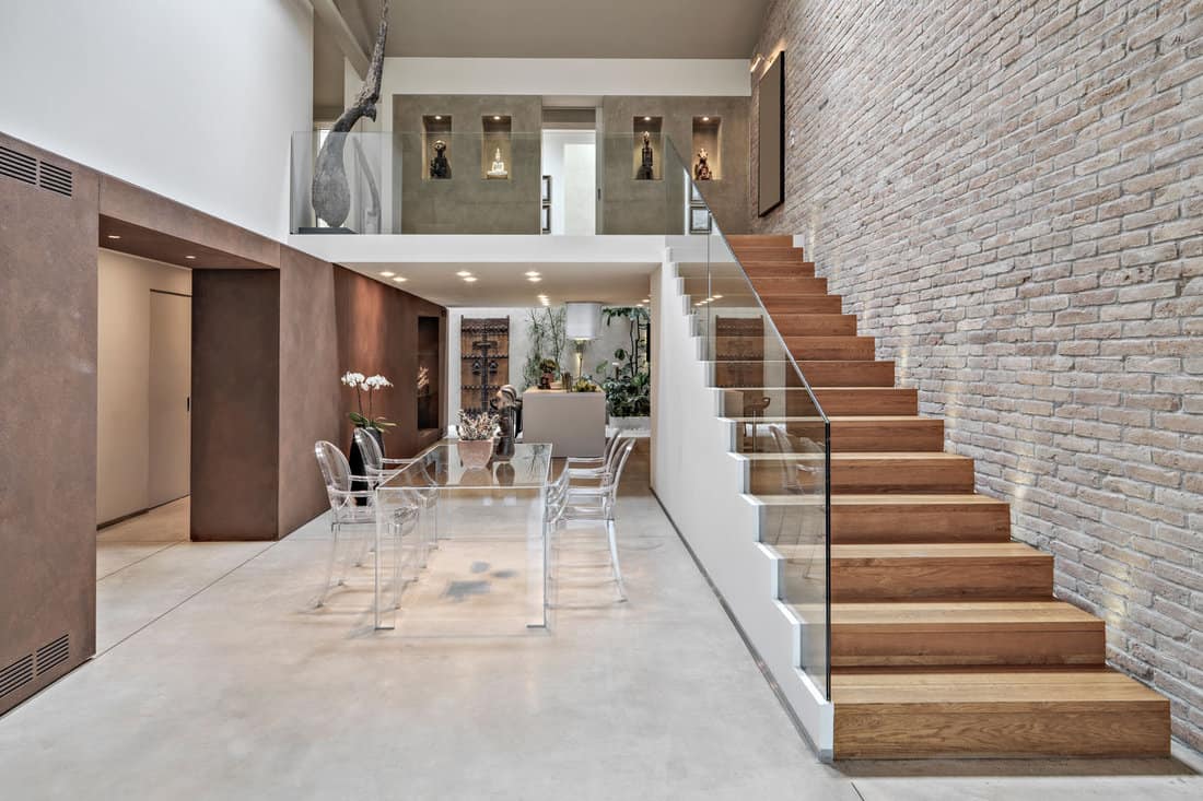 interior shots of a modern loft, in foreground the dining table with its chairs to whose right there is a wooden staircase the walls are covered of bricks 